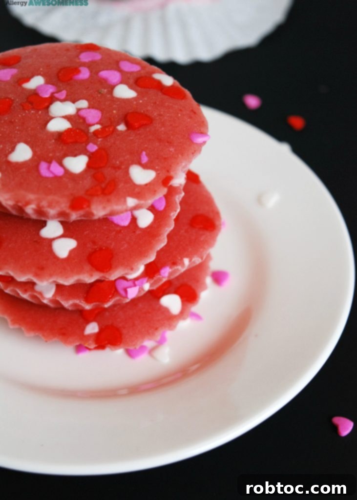 A child's hand holding a heart-shaped dairy-free frozen strawberry yogurt bite, adorned with a few sprinkles, against a blurred background