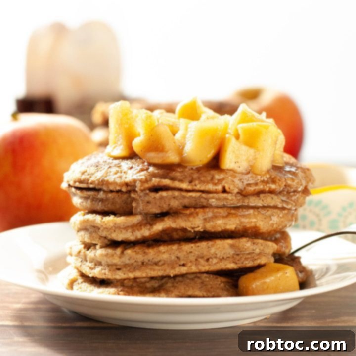 Stacked spiced apple oatmeal pancakes, garnished with fresh apple slices and a sprig of rosemary.