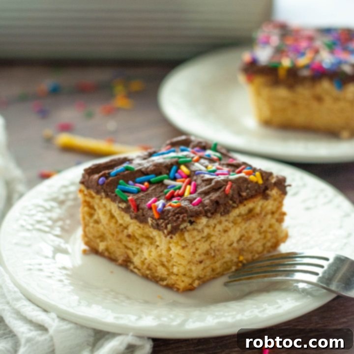 A single slice of gluten-free vegan yellow cake with chocolate frosting and sprinkles on a white plate, ready to be served.