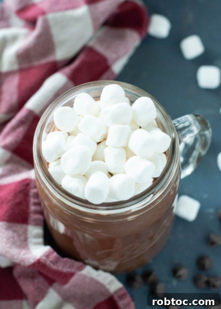 A festive mug of dairy-free slow cooker hot cocoa, topped with marshmallows and a candy cane.