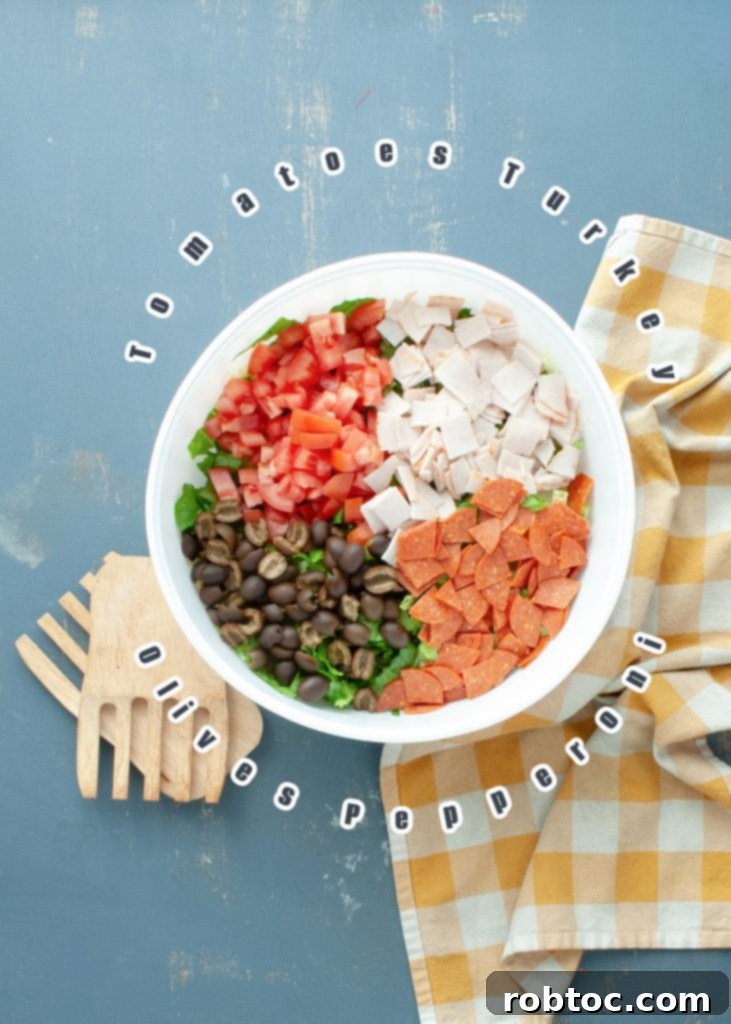 overhead view of unmixed Italian chopped salad with ingredients separated and labeled, including pepperoni, turkey, tomatoes, olives, and pepperoncini