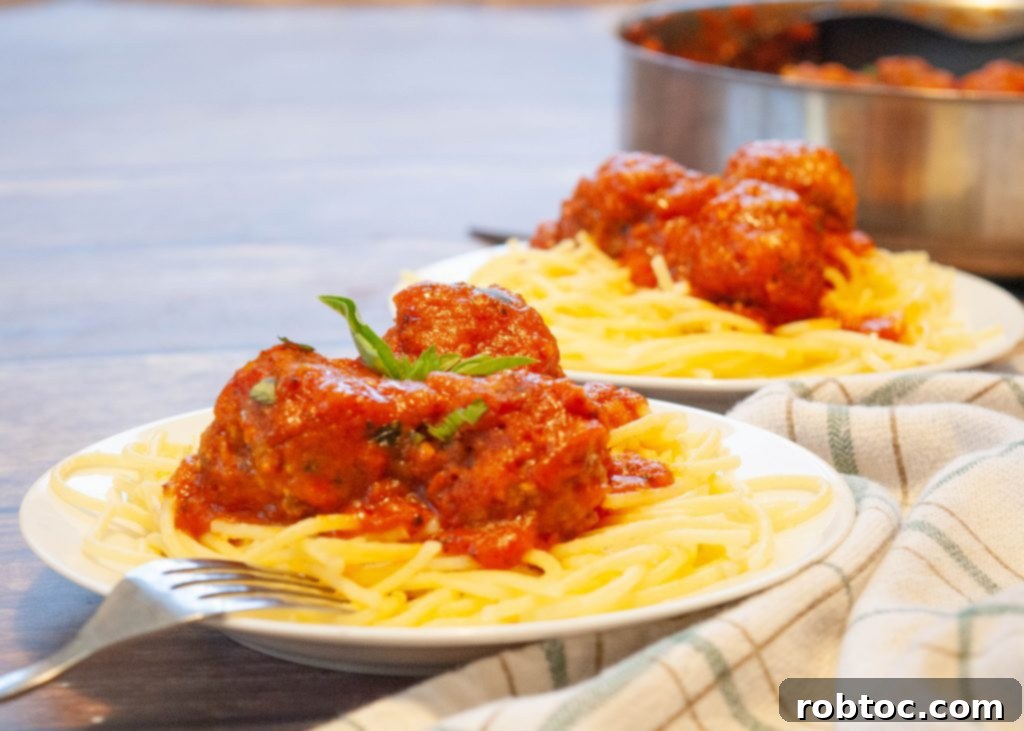 Two plates of gluten-free spaghetti topped with juicy meatballs, garnished with fresh basil
