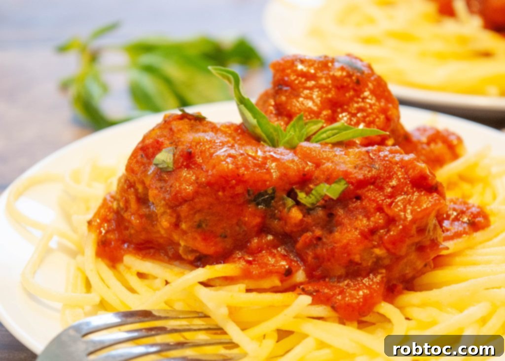 Close-up of a white plate with gluten-free pasta topped with meatballs and fresh basil