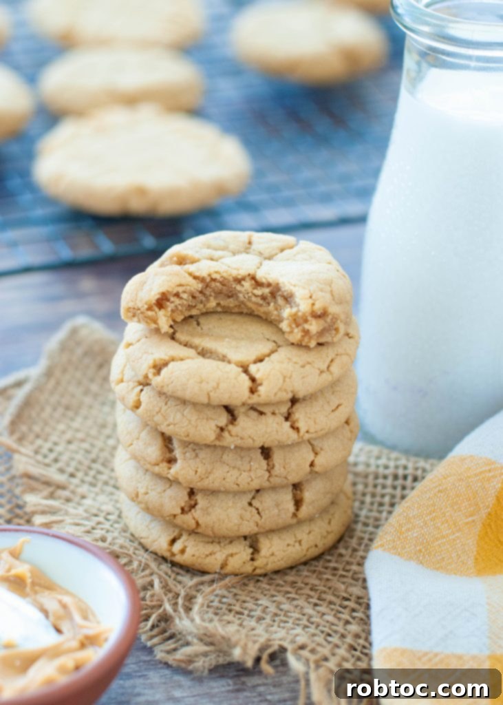 Easy Gluten-Free Peanut Butter Cookies 4 A stack of several gluten-free peanut butter cookies on a white plate, with one cookie having a bite taken out, revealing its soft, chewy interior.