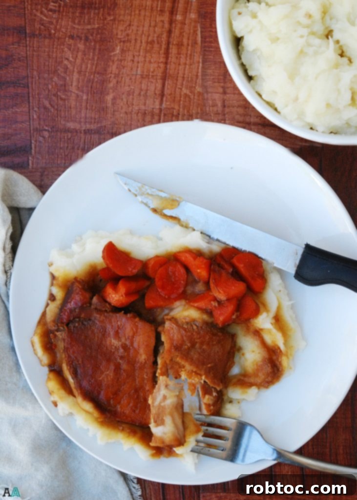Serving of Slow Cooker San Francisco Pork Chops with carrots and a generous pour of the savory glaze over mashed potatoes.