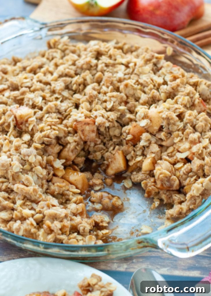 Quick and Easy Gluten Free Apple Crisp 5 A slice of warm gluten-free apple crisp has been removed from a glass pie plate, revealing the tender, spiced apple filling beneath the golden crumble topping.