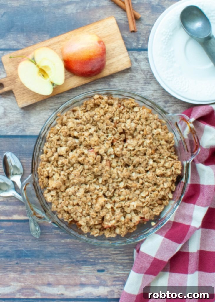 Quick and Easy Gluten Free Apple Crisp 6 Top-down view of a gluten-free apple crisp in a glass pie plate, with fresh apples arranged neatly beside it on a rustic surface, highlighting the ingredients.