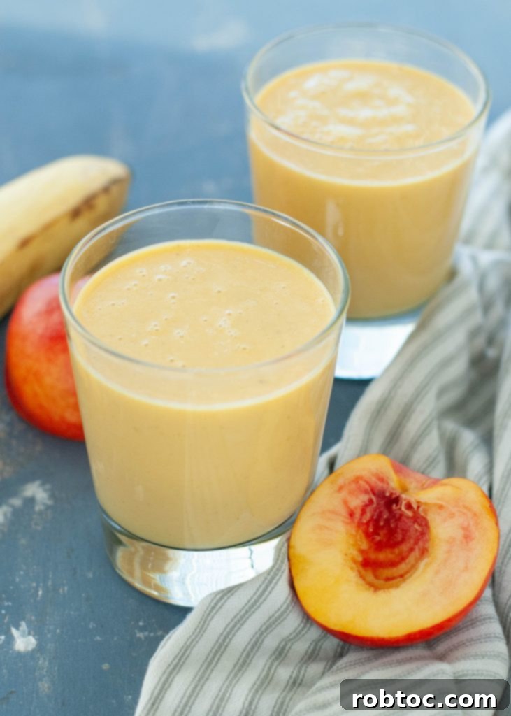 Two glasses of dairy-free peach protein smoothie with fresh fruit garnishes, showcasing a vibrant and healthy breakfast option.